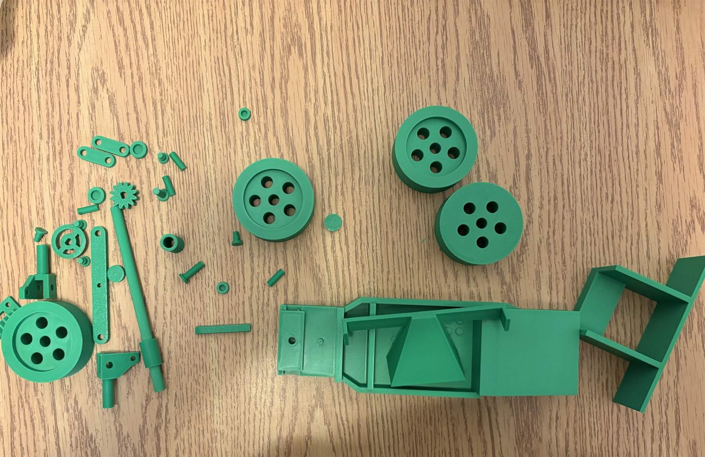 Green PLA racecar parts laid out on a table before assembly