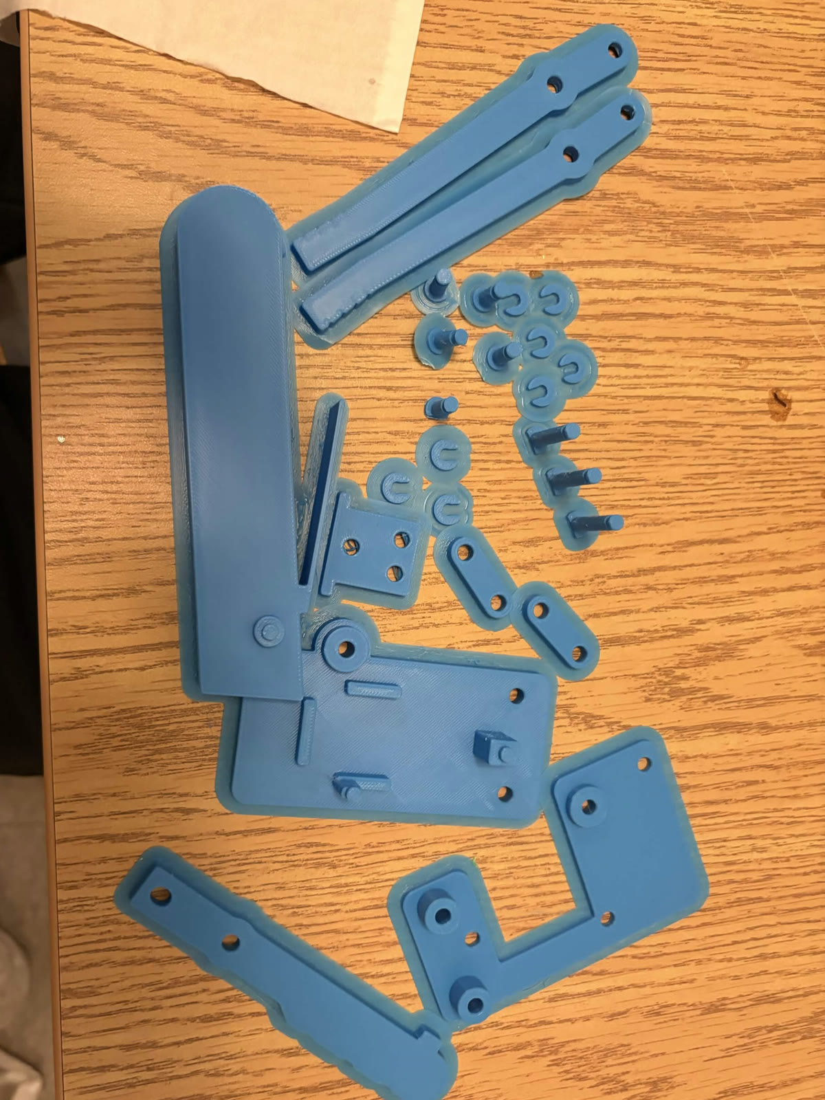 Blue PLA gripper parts fresh off the print bed: handle, jaws, links, plates, pins and clips