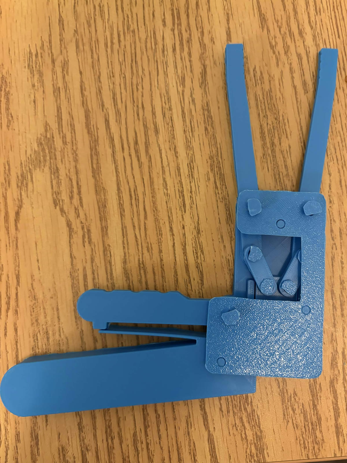 Assembled blue PLA snack gripper prototype on a wooden table, jaws open